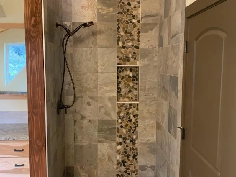 Walk-in tile shower with pebble accent band and mosaic floor